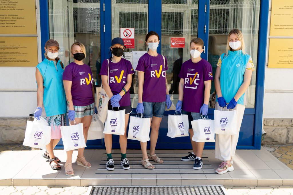 Katya (right) and 5 other volunteers prepare to deliver lunches. They stand with bags and wear protective masks and gloves.