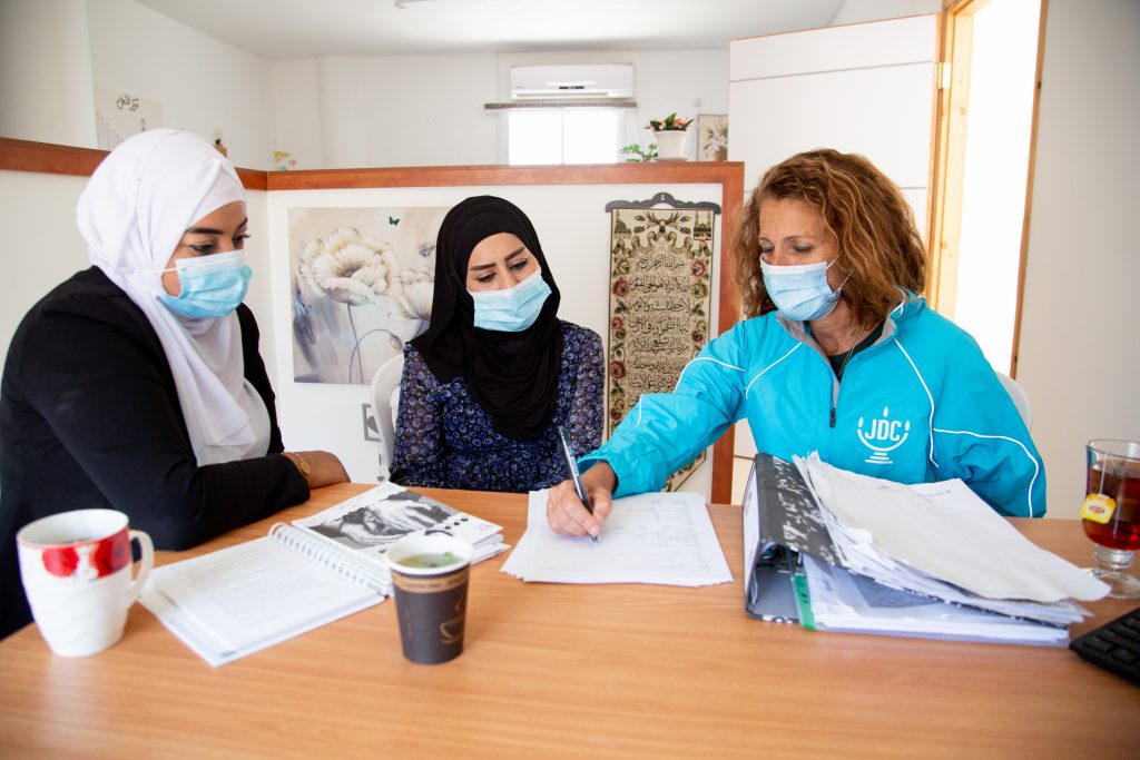 Ziva (right) sits with two Arab Israeli women, helping them fill out forms.