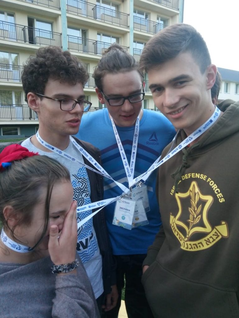Andrew (center) stands with 3 AJT friends at an AJT seminar. Their lanyards are tangled, and everyone is laughing about it.