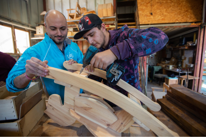 JDC volunteer in Israel helps young man in baseball hat with woodwork.