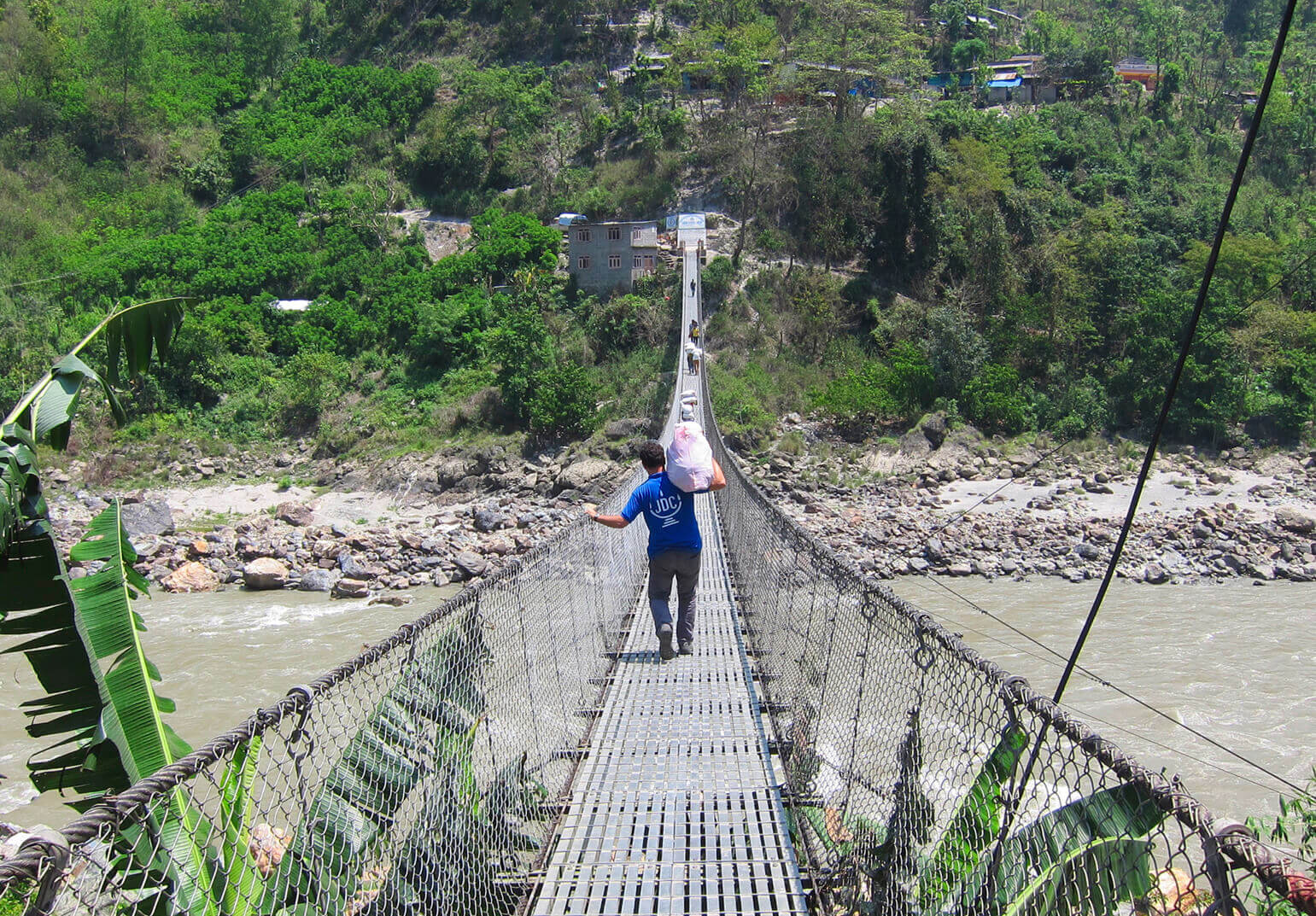 JDC aid worker carrying a large white package over his shoulder while crossing a rope bridge.