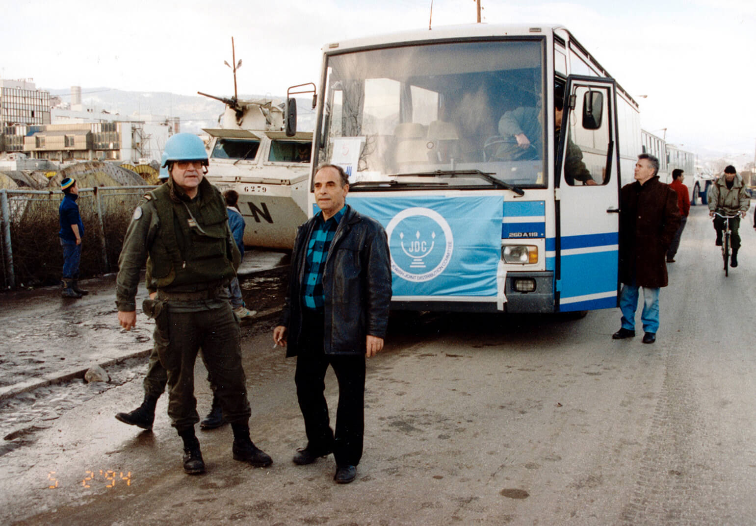 In Sarajevo, Bosnia & Herzegovina, a man stands outside a bus adorned with a blue JDC banner during the Siege of Sarajevo in 1994.