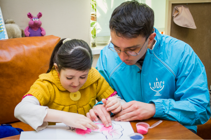 JDC volunteer in the former Soviet Union helping a young girl draw a pink flower.