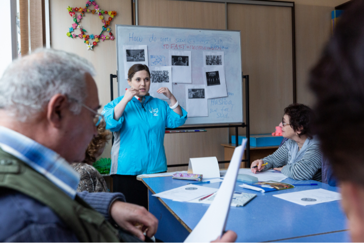 JDC volunteer standing at the head of a table during a workshop.