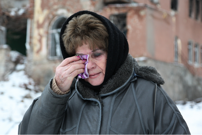 A Jewish woman in a winter coat dabbing her eye in Eastern Ukraine while it’s snowing outside.