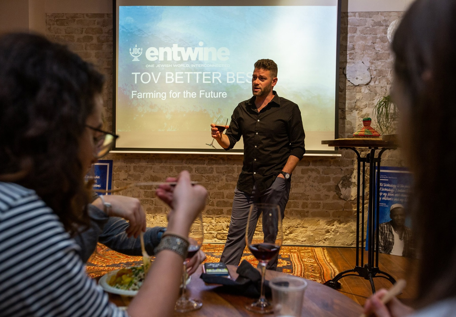 JDC Entwine speaker holding a glass of red wine while presenting on Tikkun Olam Ventures (TOV).