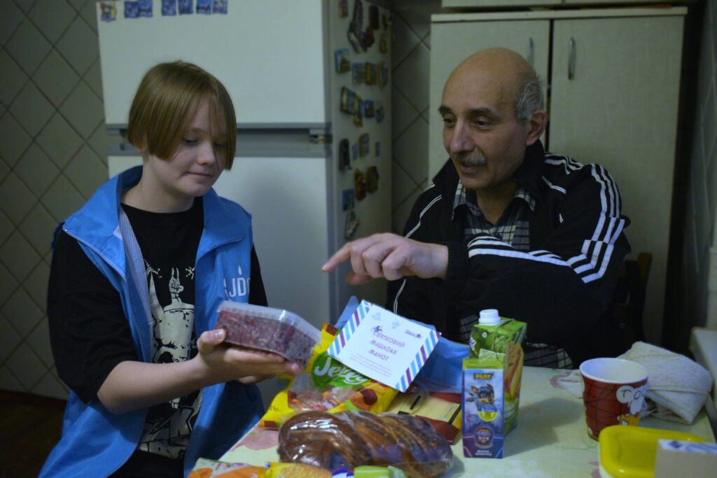 A young JDC volunteer delivers mishloach manot to an elderly community member in Zaporizhzhia, Ukraine.